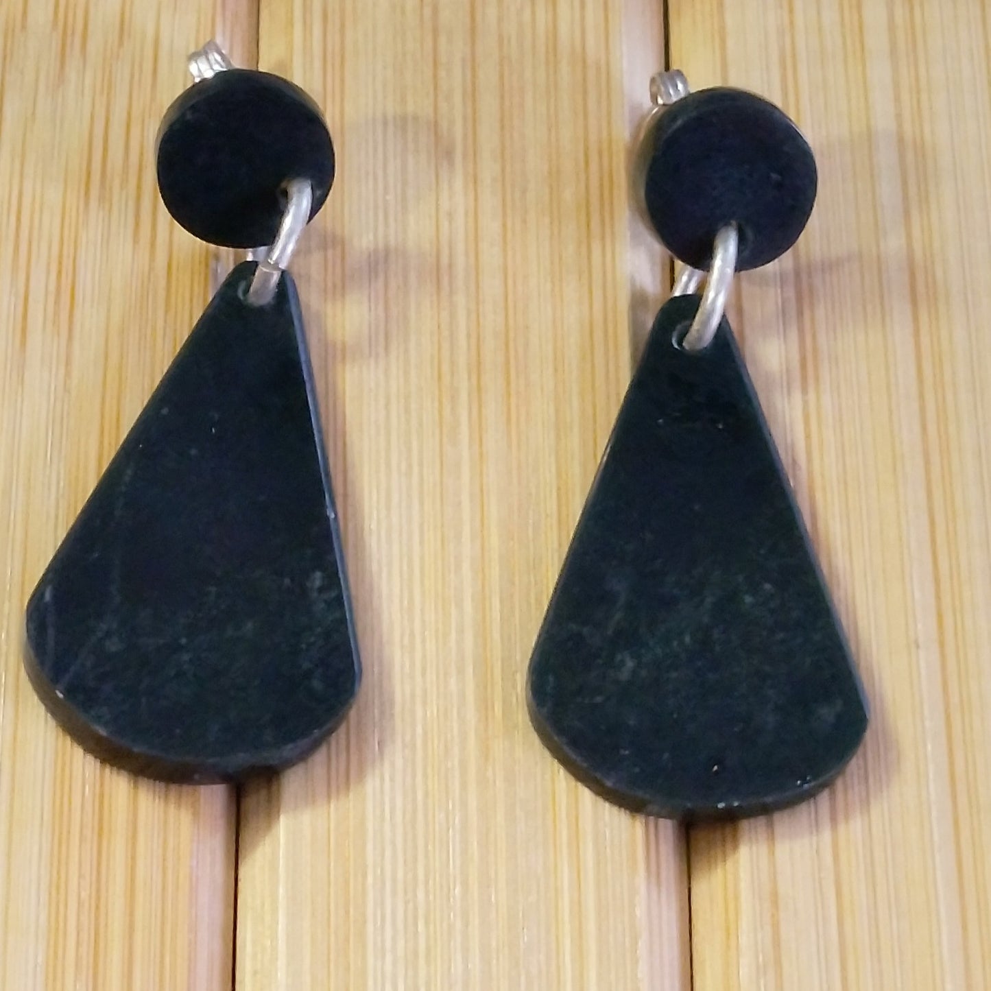 Modern drop style black jade and sterling silver stud earrings on wooden background.